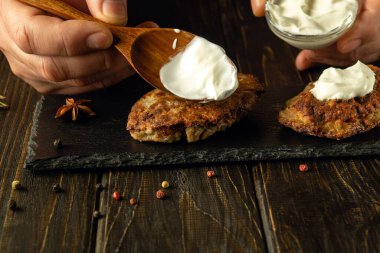 Şefin elinde ekşi krema olan bir kaşığın yakın çekimi. Öğle yemeği için pirzola ve ekşi krema hazırlıyorum. Restoranda et servisi yapma kavramı.