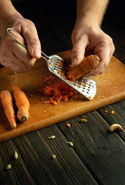 Mutfak masasında sebze yemeği hazırlama fikri. Şefin elleri kesme tahtasındaki havuçları rendeliyor..