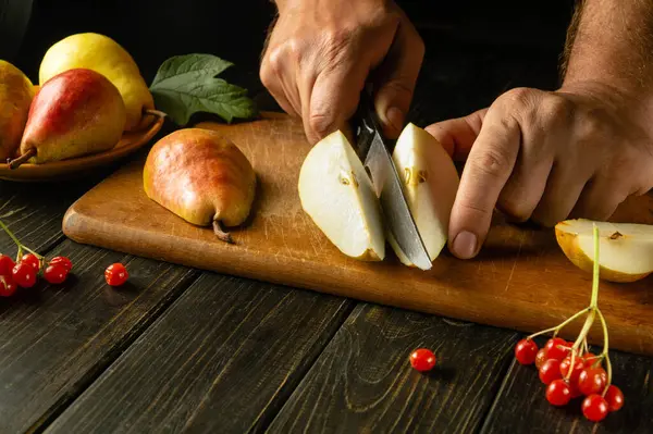 The chef cuts a pear with a knife on a cutting board to prepare compote or fruit juice. The concept of a pears diet based on a set of vitamins. Work environment on the kitchen table.