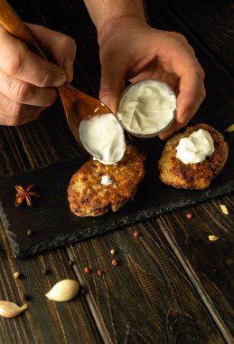 Şef pirzolalara tatları için bir kaşıkla ekşi krema ekler. Öğle yemeği için et yemeği hazırlama kavramı.