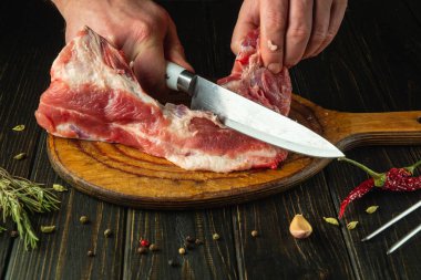 Lokantada mutfak masasında yemek hazırlamadan önce aşçının eli bıçakla çiğ et kesiyor..