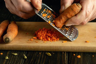 Mutfak masasında havuç rendeleyen bir şefin yakın çekimi. Sağlıklı beslenme ve sebze diyeti kavramı.