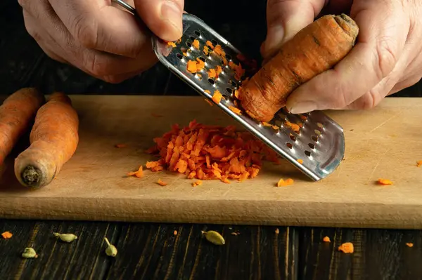 Mutfak masasında havuç rendeleyen bir şefin yakın çekimi. Sağlıklı beslenme ve sebze diyeti kavramı.