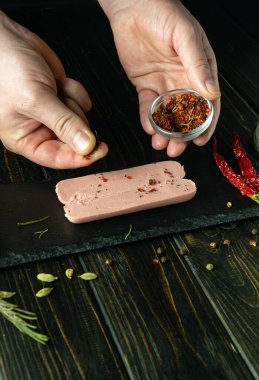 Aşçı mutfak masasında baharatlı aromatik sosis hazırlar. Şef pişirmeden önce çiğ sosise kuru baharat ekliyor..