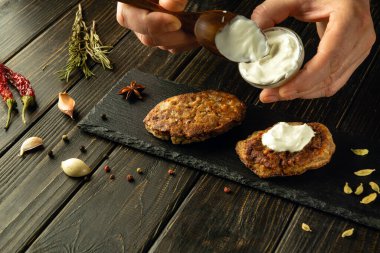 Aşçı pirzolalara tadı için bir kaşıkla ekşi krema ekler. Kahvaltıda et yemeği pişirme kavramı. Reklam alanı