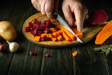 Mutfak kesme tahtasındaki haşlanmış sebzeleri kesmek için bıçak kullanan bir adamın ellerine yakın çekim. Venegret veya Ukrayna ulusal yemeği pişirme kavramı.
