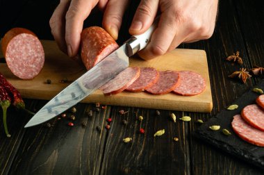 Barda et masası servis etmek için mutfak tahtasındaki salam sosisini dilimlemek. Şef 'in elinde bıçak..