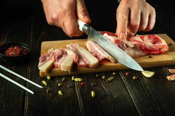 Stock image The process of preparing sandwiches for a snack from lard and garlic in the public house kitchen. Chef hands use a knife to cut pork lard on a wooden cutting board.