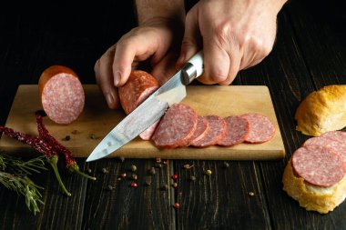 Mutfak masasında et sosisi dilimleyen bir aşçının elindeki bıçak. Atıştırmak için sandviç yapmak gibi basit bir kavram..