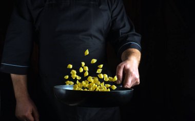 Şef, mutfak yemek odasındaki tavada makarna pişiriyor. Lezzetli makarna yapmak için basit bir fikir. Reklam için siyah alan.