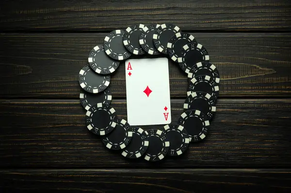 stock image Playing card ace of diamonds with black chips from winning on a vintage table in a clubhouse. Low key concept of luck symbol in poker game.