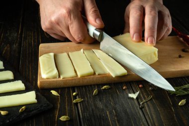 Mutfak tahtasında mozzarella peyniri dilimliyorum. Aşçının elinde bir bıçak var. Halk evinde peynir tabağı servis etmenin gösterişsiz bir konsepti..