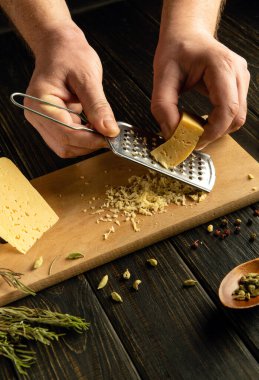 Aşçı mutfak masasında öğle yemeği hazırlamak için sert peynir rendeliyor. Peynir yemeği hazırlamak için gösterişsiz bir konsept.