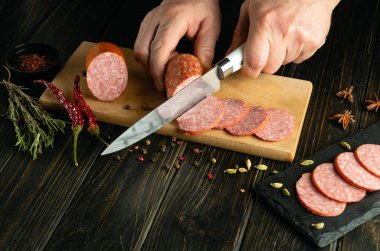 Kesme tahtasında sosis dilimlemek. Öğle yemeği ve atıştırmalık servisi için bir aşçının elinde bıçak..