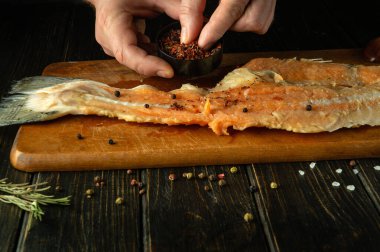 Aşçı ellerini mutfak masasındaki çiğ balık filetosuna kuru aromatik baharatlar eklemek için kullanır. Restoranın mutfağında ringa balığı hazırlama kavramı.