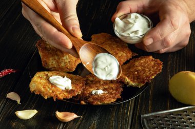 Bir adamın elinde ekşi krema olan tahta kaşığın yakın çekimi. Patatesli krep ve ekşi kremayla öğle yemeği hazırlıyoruz. Handa yemek servis etmenin gösterişsiz bir yolu..