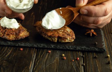 Mutfak masasındaki aşçının elleriyle ekşi kremayla pirzola pişirmek. Ekşi kremalı aşçının elinde kaşık.