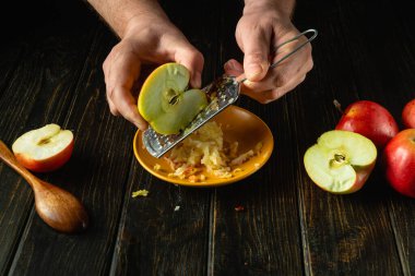 Elmaları rendelemek için el rendesi kullanmak. Mutfak masasında elma püresi hazırlayan bir adamın yakın çekimi. Ücretsiz reklam alanı.