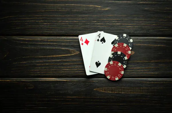 A combination of playing cards from one pair and winning chips on a black vintage table. Low key concept of a modest winning combination in a poker club or casino.
