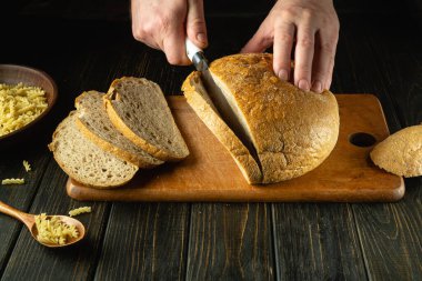 Bir fırıncı kahvaltı için mutfak tahtasındaki bıçakla taze ekmek keser. Sağlıklı beslenme ve geleneksel fırın ürünleri kavramı. Reklam alanı.