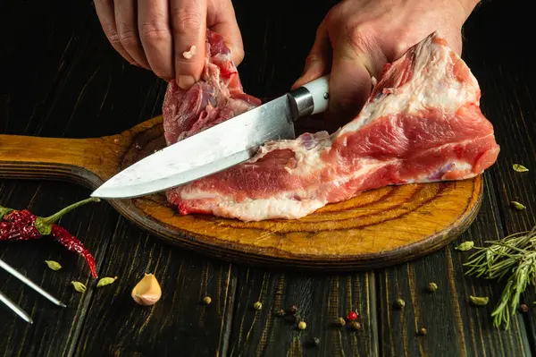 A butcher cuts meat with a knife. Cutting pork ribs by a chef\'s hands on a kitchen table before preparing a fatty dish.