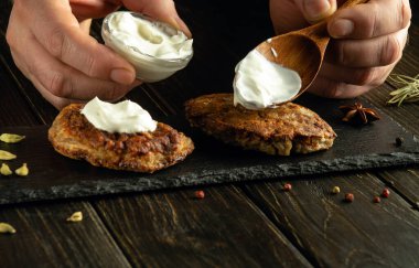 Kahvaltıdan önce et pirzolasına ekşi krema eklemek için kaşıkla yemek yapan bir elin yakın çekimi..