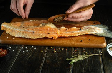 Mutfak masasında balık bifteği pişirmek. Kaşık ve kişniş aşçının elinde..