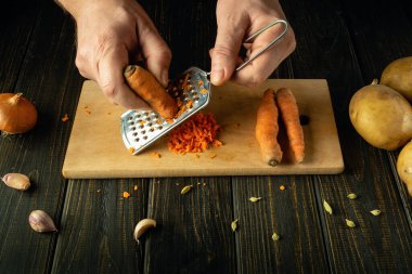 Evdeki mutfakta yemek pişiren adam. Kırpılmış erkek eli görüntüsü rendeleyiciye havuç sürer. Mutfak sağlıklı yeme konsepti.