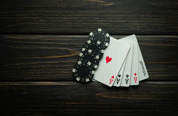 Card combination five of a kind aces and winning chips on a black table. Low key concept of major winning combination in poker club or casino.