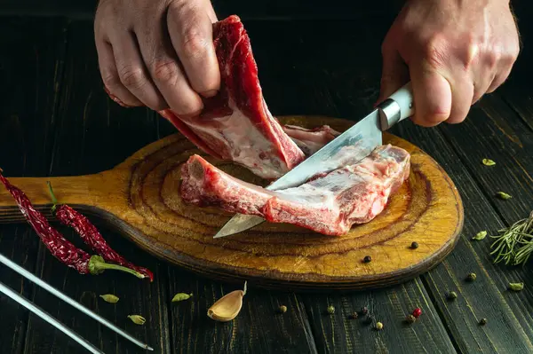 Chef hands with a knife cutting meat on a kitchen cutting board. Low key concept of preparing a meat dish for lunch.