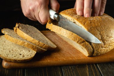 Mutfak kesim tahtasına çavdar ekmeği kesen bir şef elin yakın çekimi. Mutfak masasında ekmek ya da sağlıklı beslenme ve geleneksel fırın ürünleri konsepti.