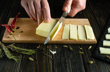 Aşçı, elinde bir bıçakla, yemek masasını servis etmek için tahta bir kesme tahtasıyla süt peyniri keser..