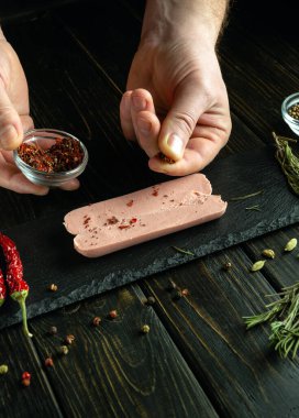 Aşçı mutfak masasında elleriyle aromatik sosis hazırlar. Izgaradan önce dilimlenmiş çiğ sosise aromatik baharatlar ekle.