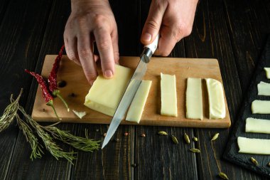 Peynir aperatifi hazırlıyorum. Mutfak masasındaki şefin elinde bıçakla peynir dilimlemek..