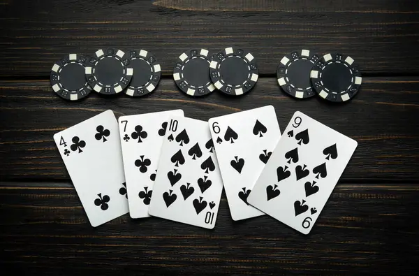 Chaotically lying playing cards and black chips on a vintage dark table in a poker club. Low key concept of an unsuccessful combination or losing in the club.