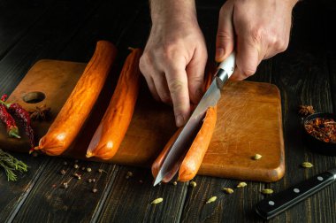 Mutfak tahtasının üzerinde tütsülenmiş sosislerden yemek pişirmek. Aşçının elinde bir bıçak..