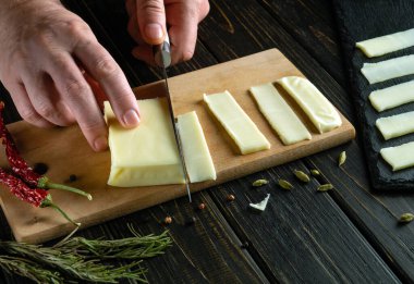 Bir restoranda sofra hazırlamak için kesme tahtasındaki şefin elinde derisi olan peyniri dilimlemek. Basit bir kahvaltı hazırlama konsepti..