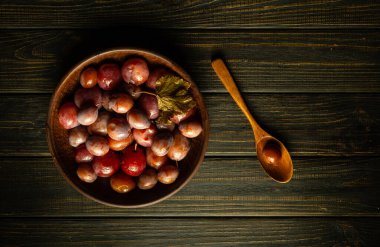 Baharatlı bir kase erik turşusu ve siyah ahşap bir masada bir kaşık. Lezzetli yemekler, vejetaryen yemek konsepti.