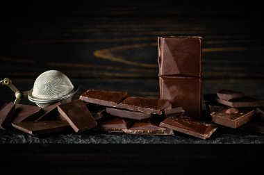 Siyah sıralama tahtasındaki kırık çikolata parçaları ve çikolata parçacıkları için mutfak süzgeci. Reklam alanı.