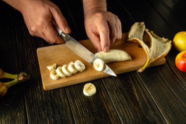 Mutfak tahtasında ince dilimlenmiş muz. Mutfak masasında bir şefin elleriyle meyve tabağı pişirmek..