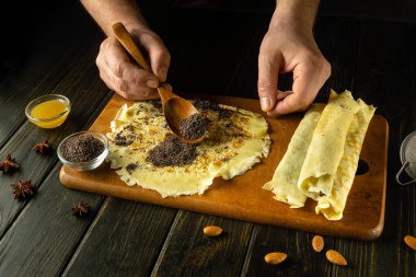 Şefin ellerinin yakın plan fotoğrafı krepe kaşıkla haşhaş tohumu ekliyor. Lokantadaki mutfak masasında haşhaş tohumu ve bal ile tatlı bir tatlı hazırlıyorum..