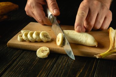 Bir şefin elinde bıçakla muz dilimlemek. Mutfak masasında meyve tabağı hazırlamak gibi basit bir kavram..