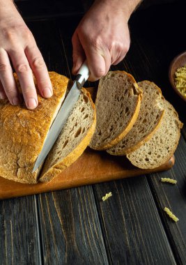 Bir şef, restoranda kahvaltıdan önce mutfak tahtasına çavdar ekmeği kesmek için bıçak kullanır..