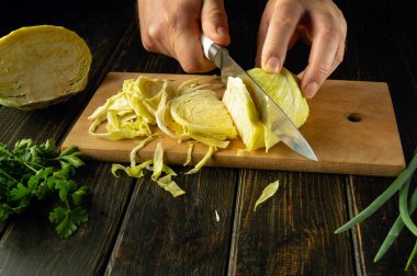 Aşçı ahşap kesme tahtasındaki bir bıçakla taze lahana keser. Restoran ya da otel için vejetaryen menüsü.