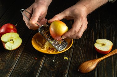 Mutfak masasında elmalı turta hazırlıyorum. Şefin elleri vejetaryen yemeği için elmayı rendeliyor..