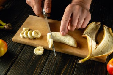 Mutfak tahtasının üzerinde ince dilimlenmiş muz. Mutfak masasında bir şefin elleriyle meyve tabağı pişirmek. Reklam için yer.