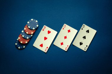 Pokerde şans, üçlü ya da set kombinasyonuyla kazanır. İskambil kağıtları ve fişler mavi bir masada bir kulüpte serilmiştir..