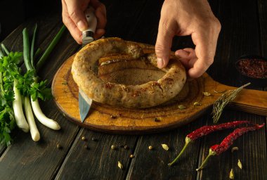 Mutfak masasında ev yapımı sosis pişirmek. Adam öğle yemeği için et sosisi kesmeden önce elinde bıçakla elini uzatıyor..