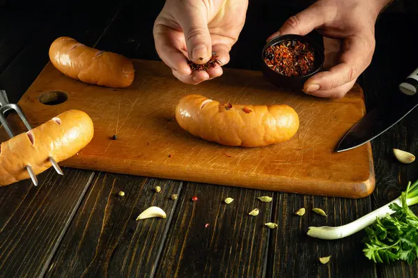 Chef hands prepare North American Vienna sausages with spices for grilling on the kitchen table.
