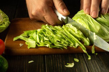 Mutfak masasında vejetaryen yemeği hazırlamadan önce taze lahana kesmek için bıçak kullanan bir şefin yakın çekimi..